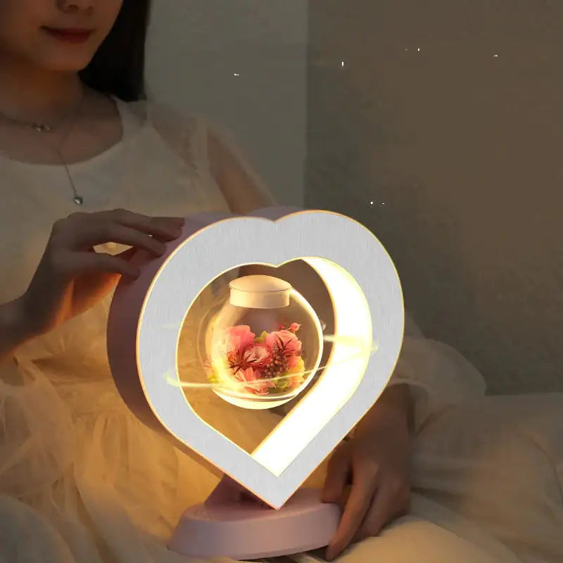 a woman holding a heart shaped lamp with flowers inside of it